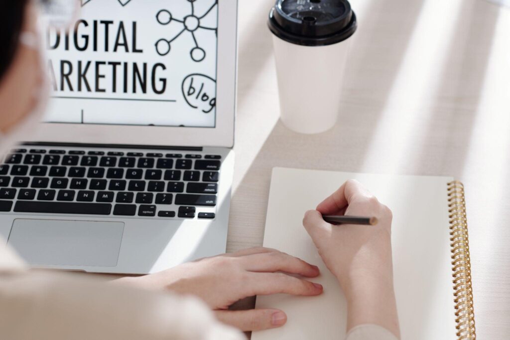 erson taking notes while studying digital marketing online on a laptop, focusing on SEO, website design, and strategy planning.